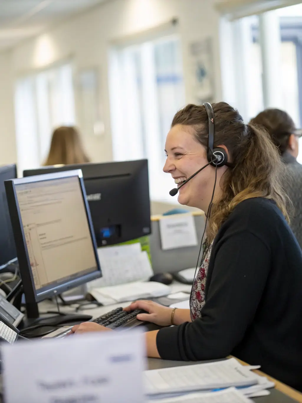 A person talking on a phone, with a headset on, in a modern office setting, assisting a client with their visa inquiries.